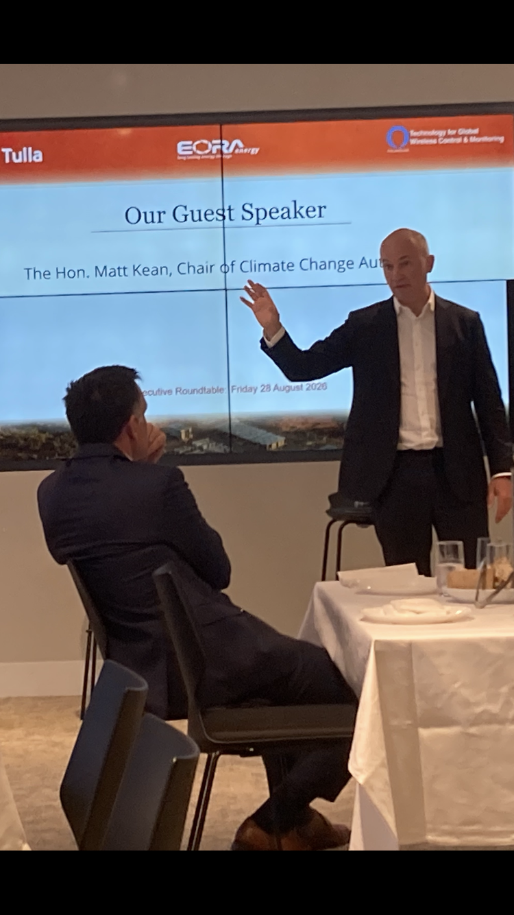 A speaker addressing guests in front of the event presentation screen